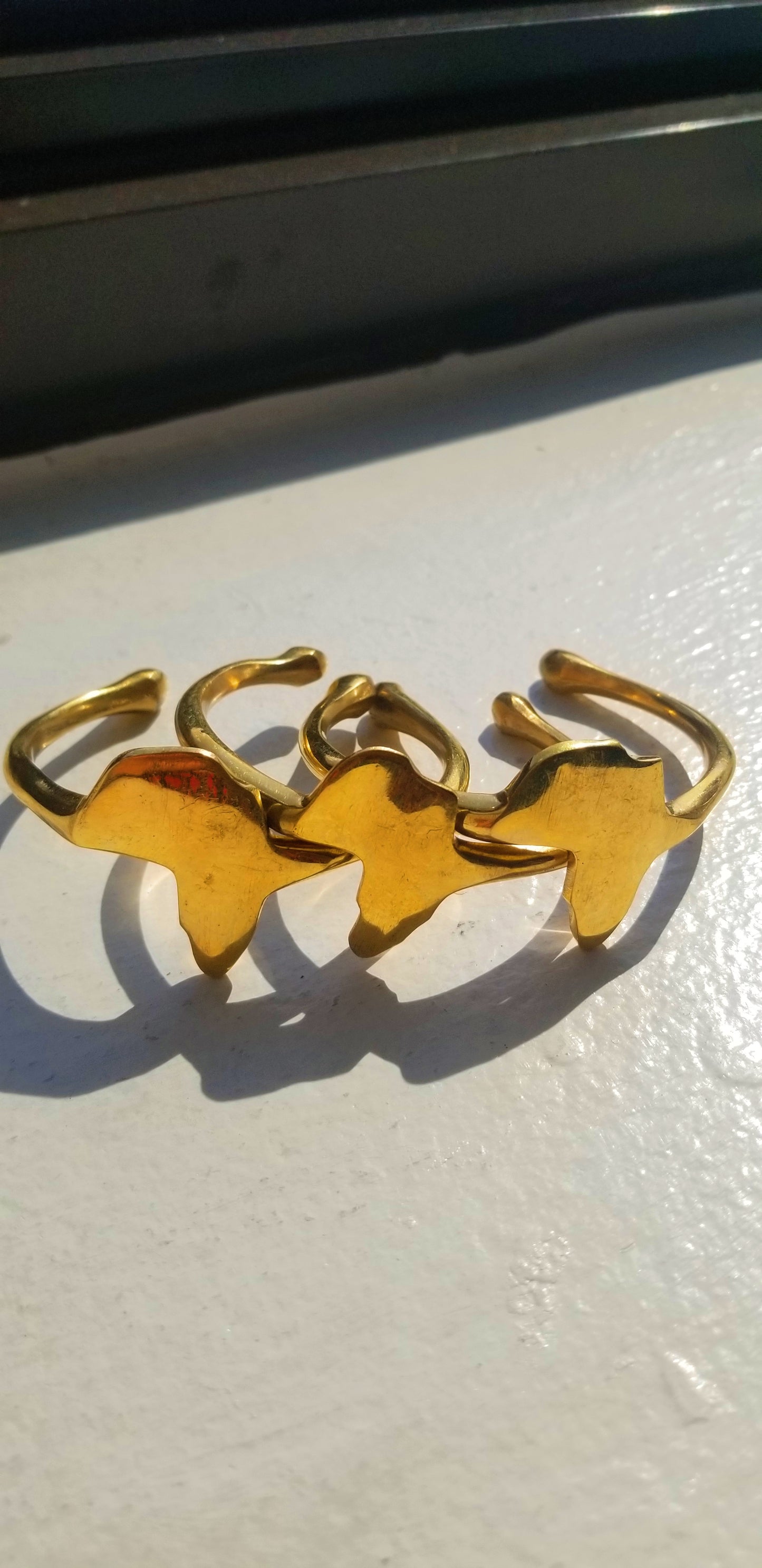 Three 18K gold plated Continent Cuffs grouped together to show high-shine finish and sculptural design consistency.