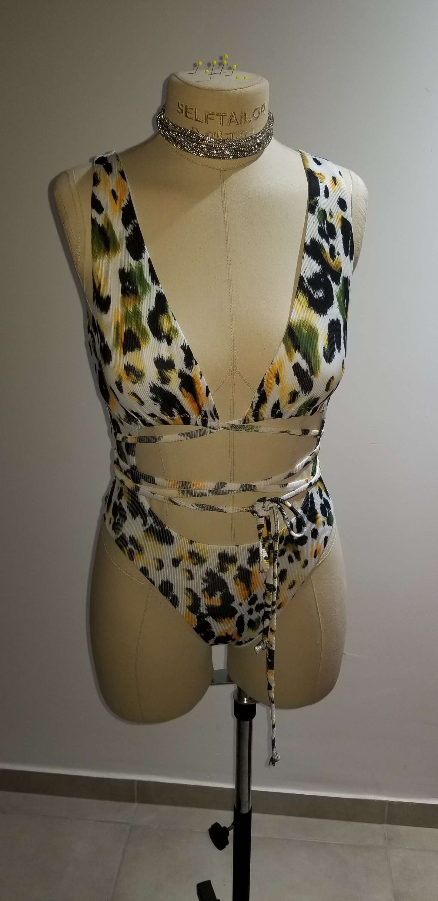 Close-up product photo of the actual emerald leopard bodysuit laying flat, showing the true green, black, and gold fabric tones.