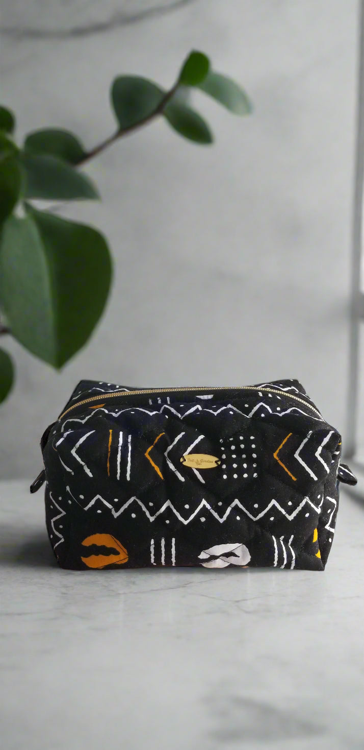 Straight-on view of the Gold & Noir tribal print makeup bag by Scope and Flow, styled on a marble vanity with a gold faucet and green plant.