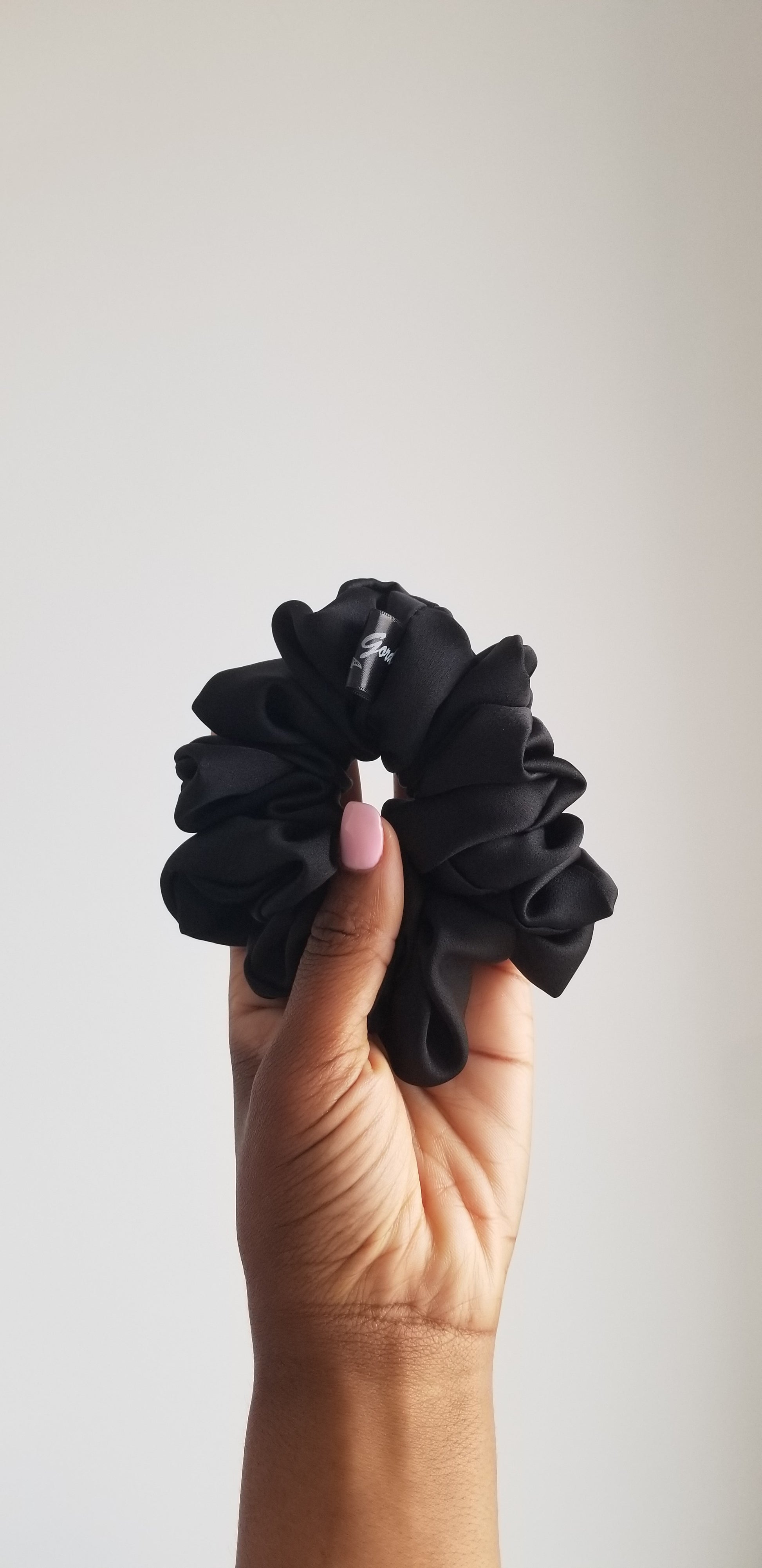 Handmade black silk scrunchie with a soft luster by Scope and Flow, styled on a white marble surface with a gold bathroom fixture.