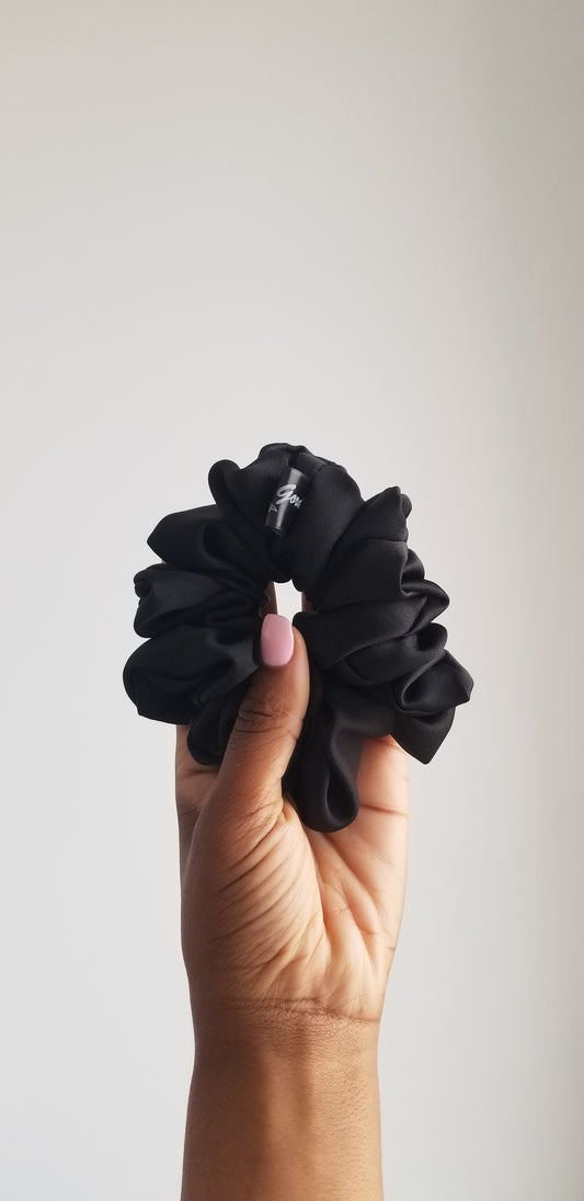 Handmade black silk scrunchie with a soft luster by Scope and Flow, styled on a white marble surface with a gold bathroom fixture.