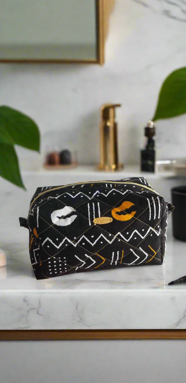 Front view of the Odyssey Noir gold and black tribal makeup bag by Scope and Flow on a marble vanity. 