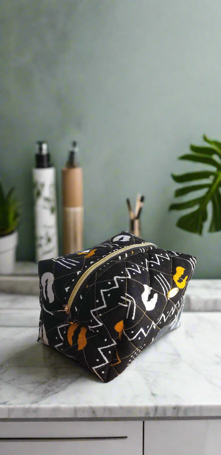 Side perspective of the handmade Odyssey Noir makeup bag styled with gold bathroom fixtures.