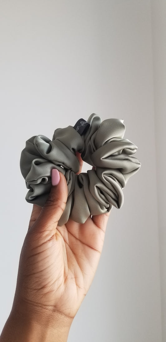 Front view of a handmade olive green silk scrunchie by Scope and Flow, styled on a white marble vanity.