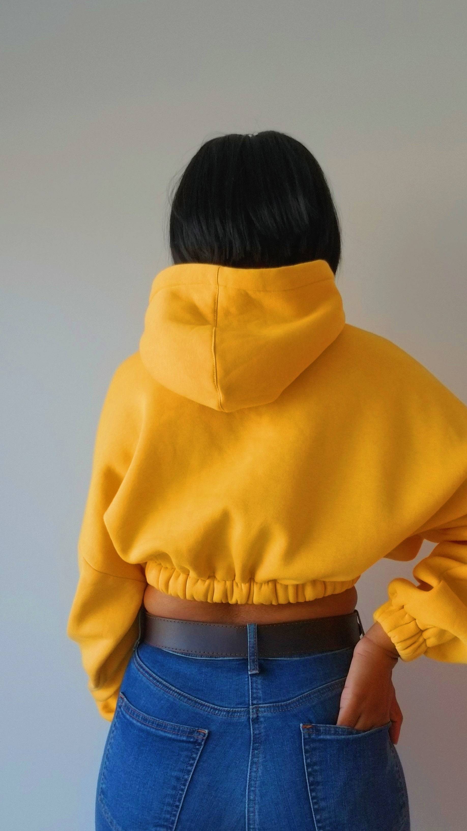 a woman wearing a yellow hoodie and blue jeans