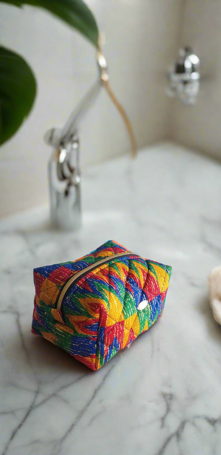 Side perspective of the handmade multicolored tribal makeup bag styled with gold bathroom fixtures.