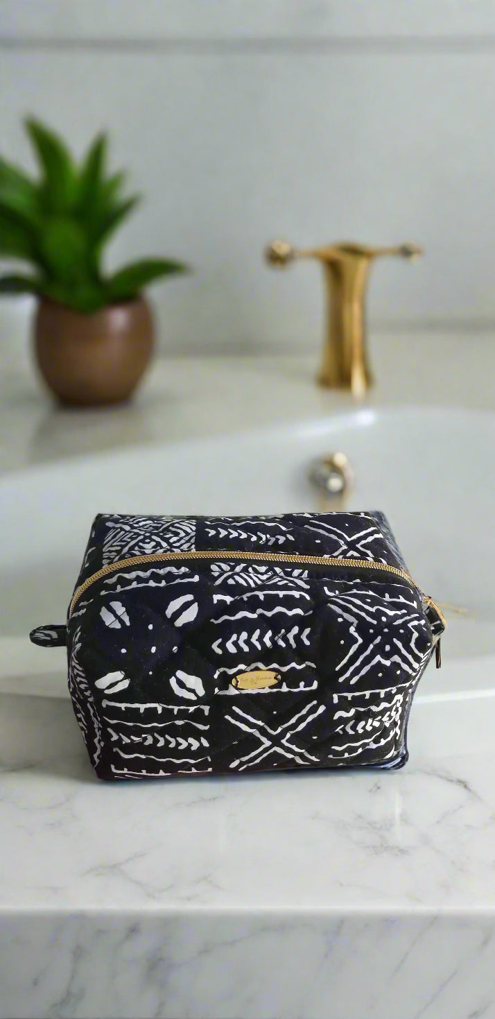 Top-angle view of a handmade black and white tribal print makeup bag with gold zipper detail, styled in a luxury bathroom.