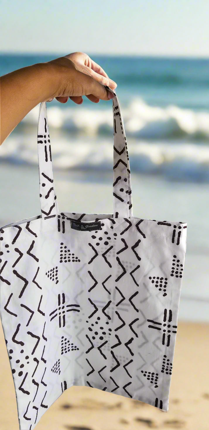 Handmade white tote bag with black tribal geometric print by Scope and Flow, pictured at the beach.