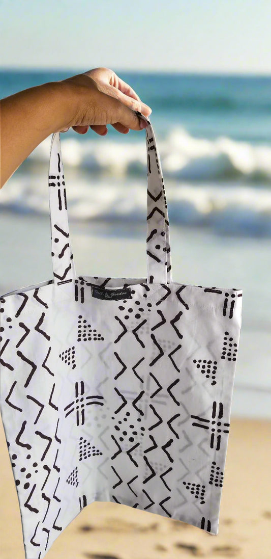 Handmade white tote bag with black tribal geometric print by Scope and Flow, pictured at the beach.