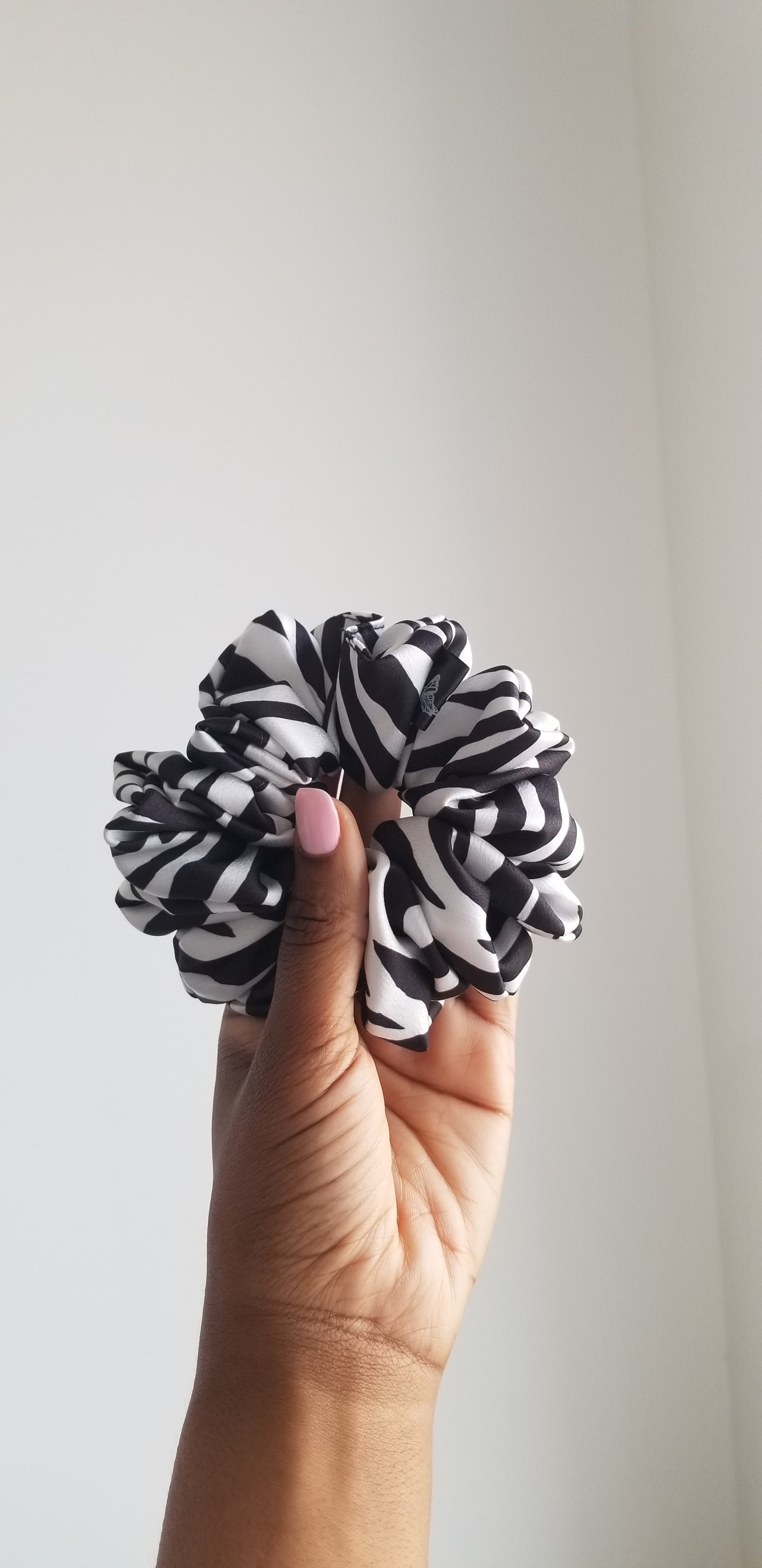 A bold black and white zebra print silk scrunchie by Scope and Flow, styled on a white marble surface.