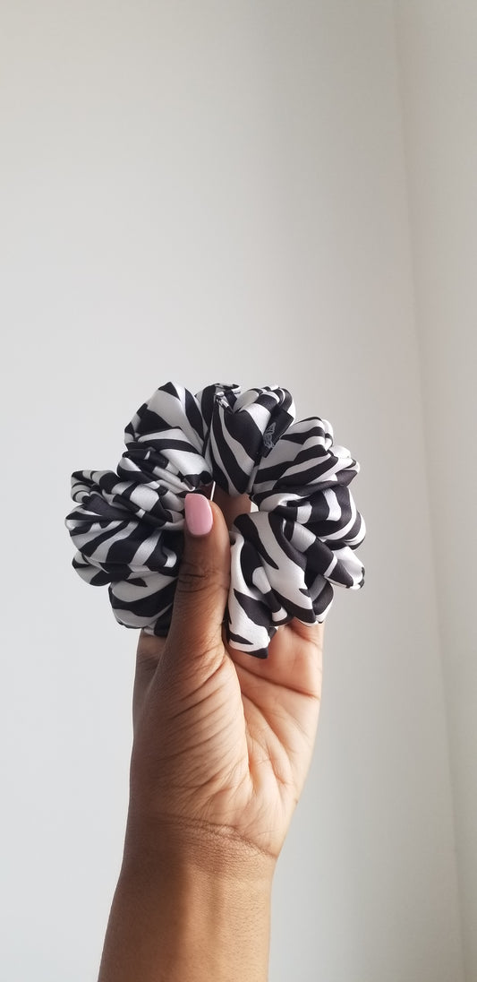 A bold black and white zebra print silk scrunchie by Scope and Flow, styled on a white marble surface.