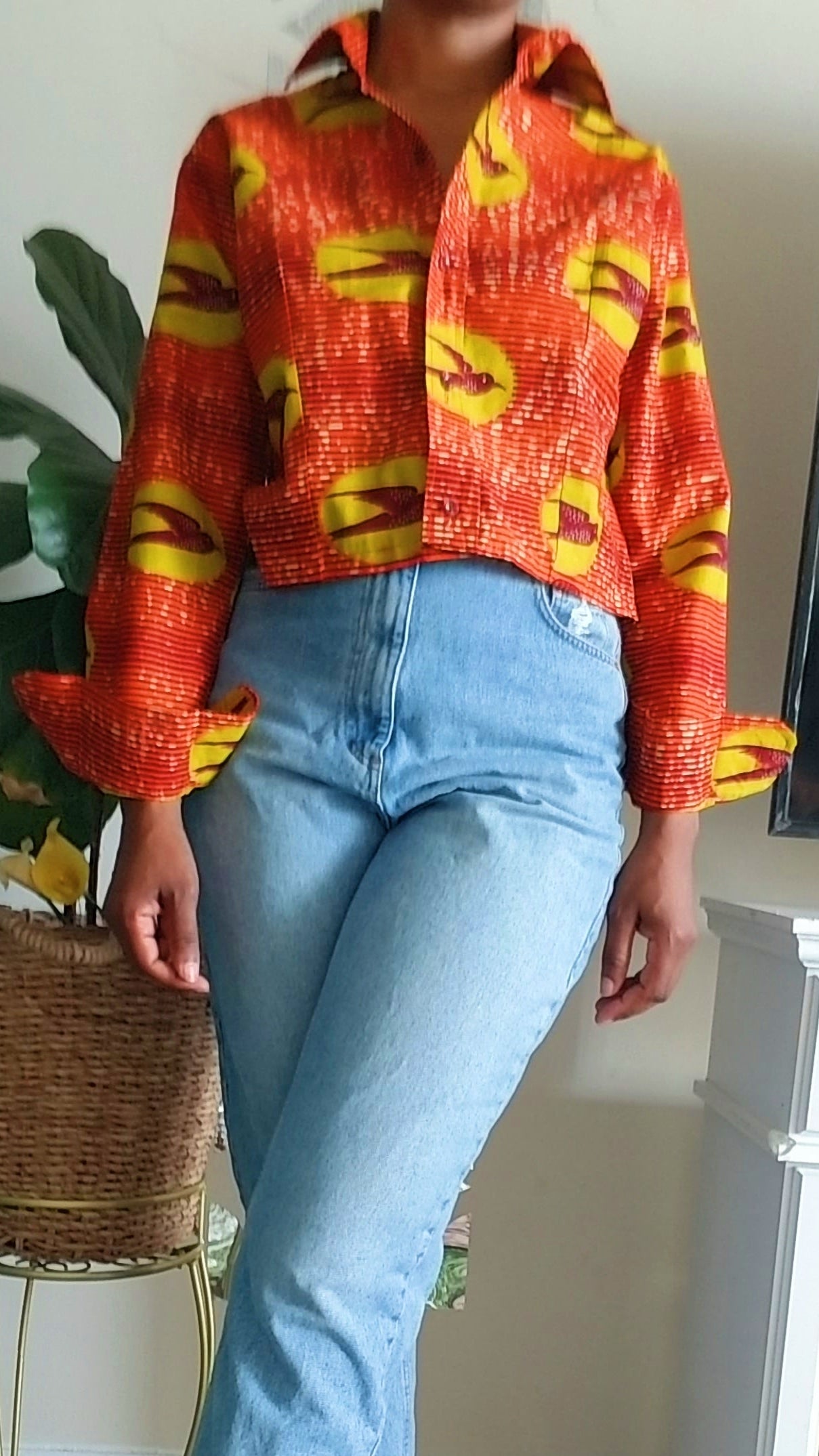 Model wearing the Scope and Flow Zola orange African print shirt in a cozy holiday living room setting.