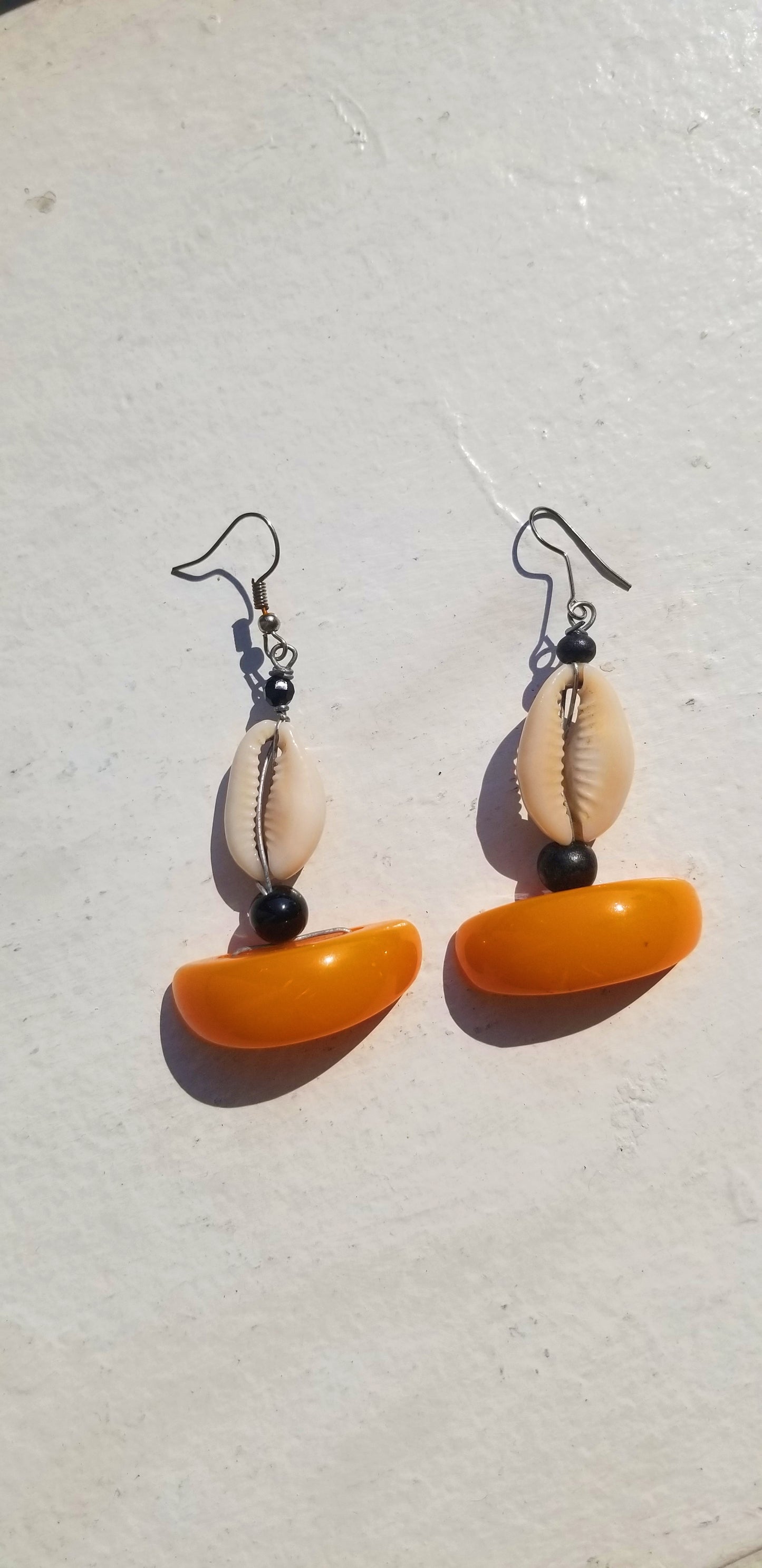 Individual pair of Amber orange resin half-moon earrings with hand-selected cowrie shell detail.